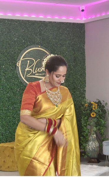 A client in a gold sari standing at the Blush Beauty Bar sign inside the salon